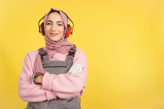 Friendly muslim female carpenter in work uniform looking at camera in studio with yellow background