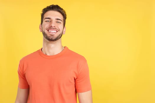 Handsome man standing with arms crossed laughing at the camera in studio with yellow background