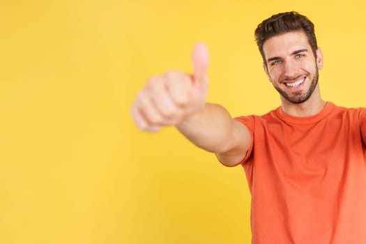 Happy caucasian man gesturing agreement raising a thumb up in studio with yellow background