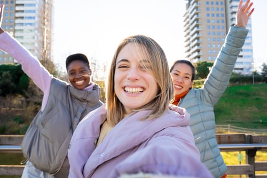 Three diverse girls taking a selfie portrait with smartphone. An Asian Chinese woman, an African and a Caucasian lady together and embracing. Friendship multi-ethnic group of real people.