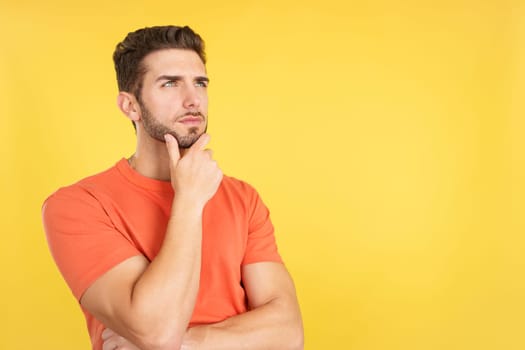 Caucasian man with hand on face and thoughtful expression in studio with yellow background