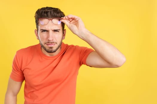 Caucasian man taking off her glasses to see in studio with yellow background