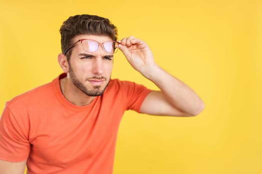 Caucasian man taking off her glasses to see far away in studio with yellow background