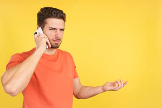 Angry caucasian man talking to the mobile in studio with yellow background