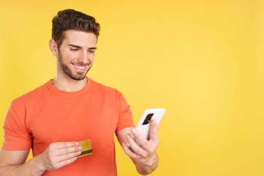 Caucasian man using the mobile and card to shopping online in studio with yellow background