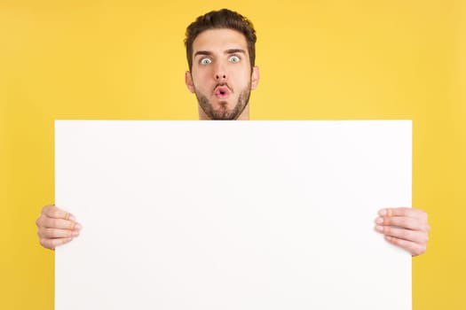 Surprised caucasian man hair holding a blank panel in studio with yellow background