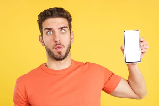 Surprised caucasian man holding a mobile with a blank screen in studio with yellow background