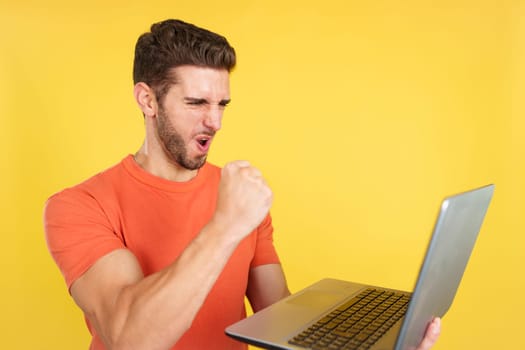 Caucasian man celebrating while looking at the laptop in studio with yellow background