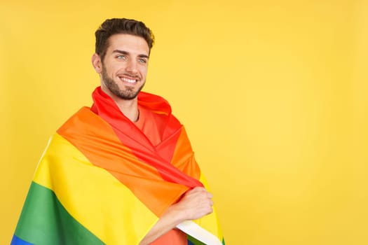 Distracted caucasian man wrapped with a lgbt flag in studio with yellow background