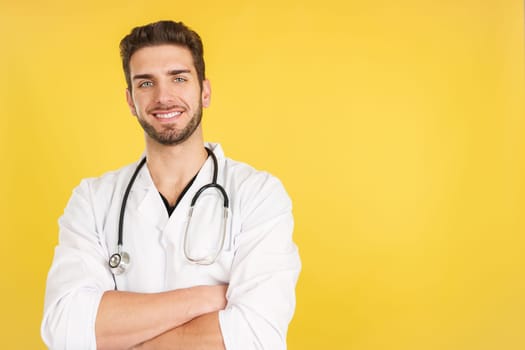 Caucasian doctor smiling at the camera with arms crossed in studio with yellow background