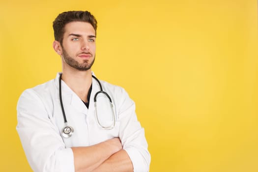 Serious caucasian doctor with arms crossed looking away in studio with yellow background