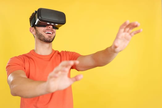 Caucasian man gesturing while wearing Virtual Reality goggles in studio with yellow background