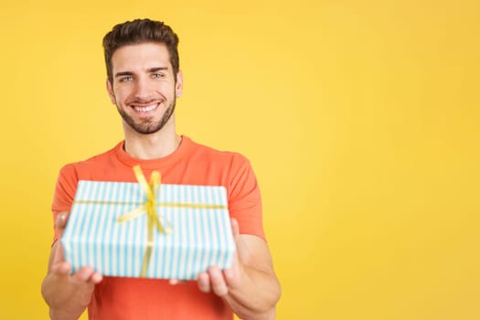 Happy caucasian man looking at the camera giving a present in studio with yellow background