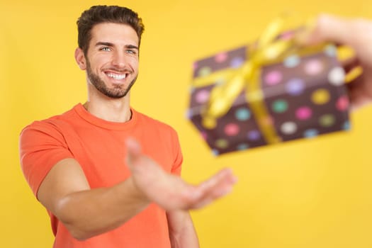 Happy caucasian man smiling while receiving a gift in studio with yellow background