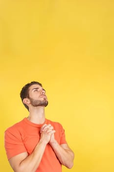 Caucasian man looking up while praying with folded hands in studio with yellow background