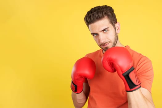 Caucasian man with red boxing gloves in fight pose in studio with yellow background