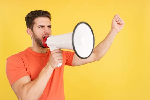 Angry caucasian man shouting using a loudspeaker in studio with yellow background