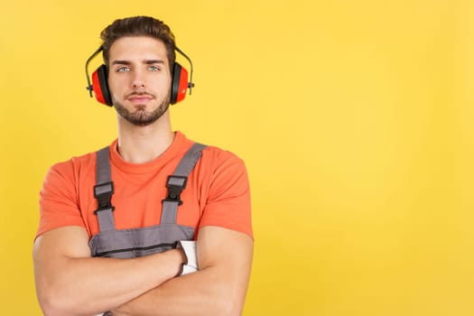 Serious caucasian worker with headphones standing with arms crossed looking at camera in studio with yellow background