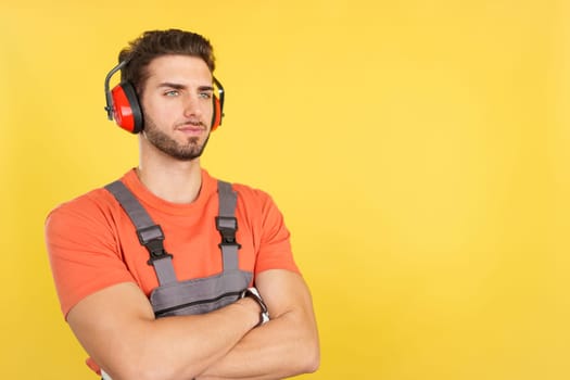 Serious worker with headphones standing looking aside in studio with yellow background