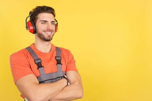 Distracted caucasian male carpenter looking away with arms crossed in studio with yellow background