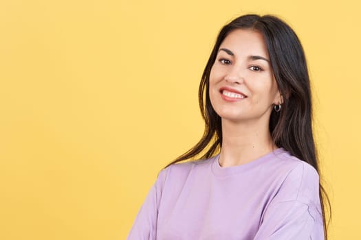 Happy hispanic woman smiling at the camera in studio with yellow background
