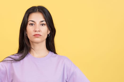 Woman looking at the camera with an angry expression in studio with yellow background