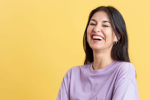 Happy hispanic woman laughing and looking at the camera in studio with yellow background