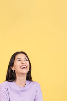 Hispanic woman laughing and looking up in studio with yellow background