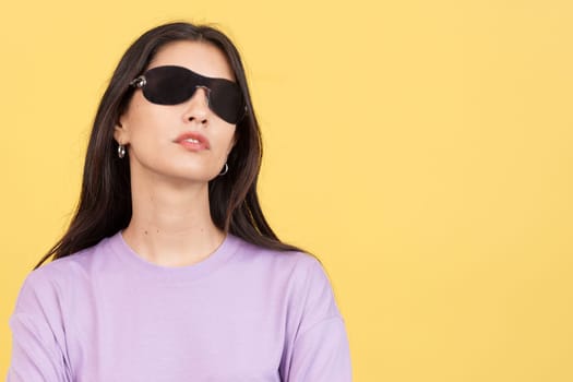 Rude hispanic woman with sunglasses looking at camera in studio with yellow background