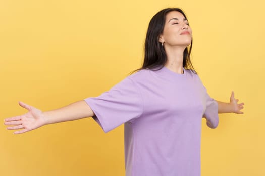 Relaxed woman with her arms outstretched gesturing wellbeing in studio with yellow background