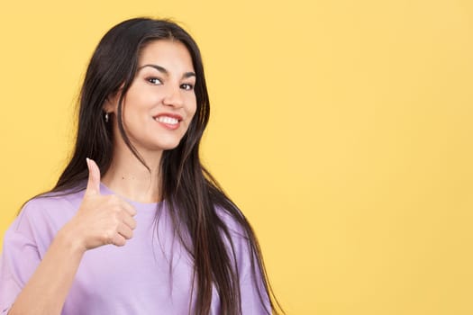 Happy caucasian woman gesturing agreement raising a thumb up in studio with yellow background