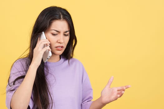 Angry caucasian woman talking to the mobile in studio with yellow background