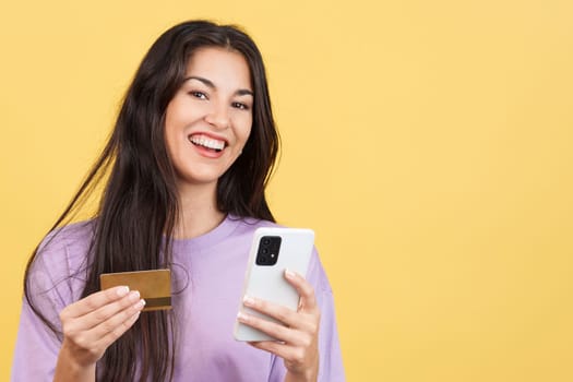Caucasian woman using the mobile and card to shopping online in studio with yellow background