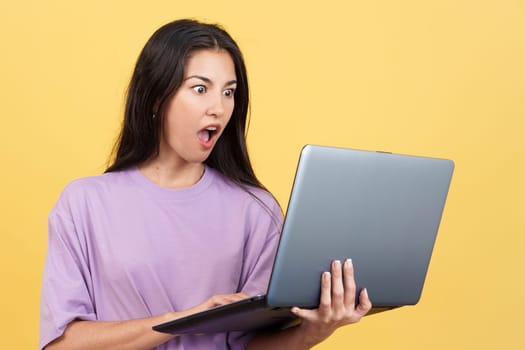 Caucasian woman with a surprised look using a laptop in studio with yellow background