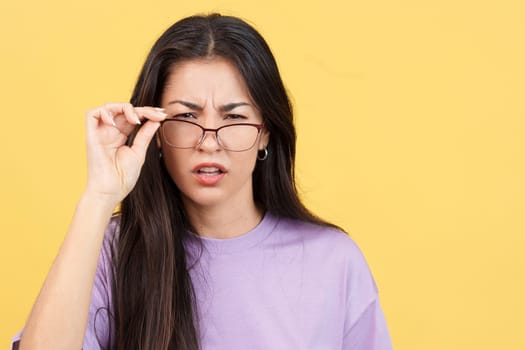 Hispanic woman taking off her glasses to see facing the camera in studio with yellow background