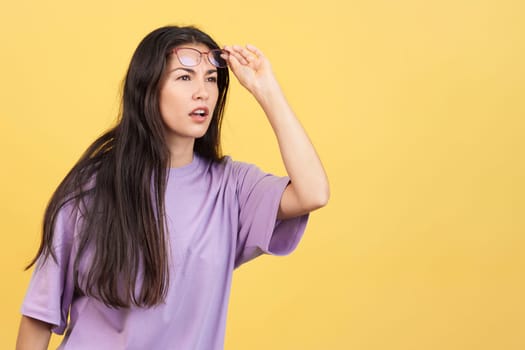 Woman taking off her glasses to see far away in studio with yellow background