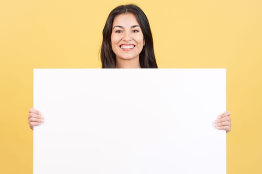 Woman holding a blank panel while smiling at the camera in studio with yellow background