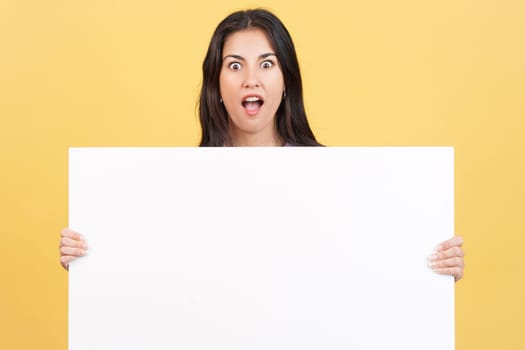 Amazed caucasian woman hair holding a blank panel in studio with yellow background