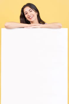 Hispanic beauty woman leaning on a blank panel in studio with yellow background