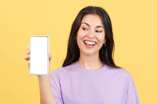 Amazed woman holding a mobile with a blank screen in studio with yellow background