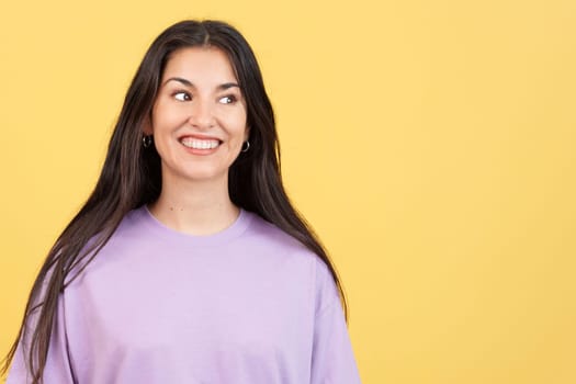 Beauty hispanic woman standing looking away while smiling in studio with yellow background