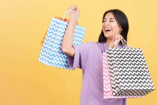 Caucasian woman raising many shopping bags while smiling and looking away in studio with yellow background