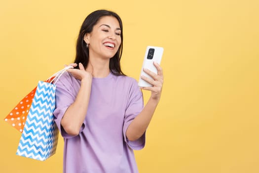 Happy caucasian woman using the mobile while holing shopping bags. Mid shot