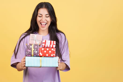 Excited caucasian beauty woman holing colorful gifts in studio with yellow background