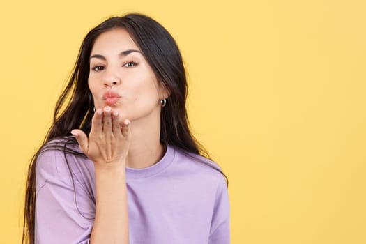 Woman blowing a kiss while looking at the camera in studio with yellow background