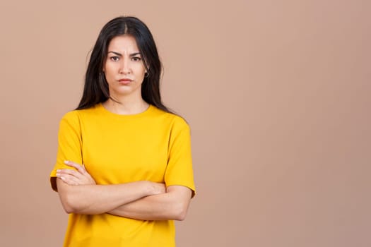 Hispanic woman crossing the arms with an angry expression in studio with brown background