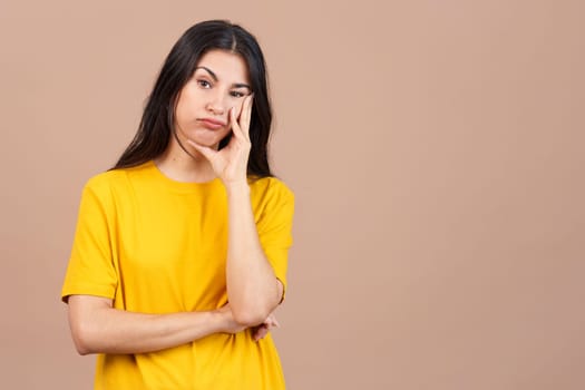 Bored hispanic woman standing and looking at the camera in studio with brown background