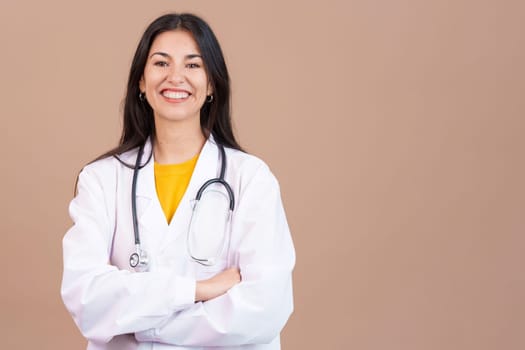 Caucasian female doctor smiling at the camera with arms crossed in studio with brown background