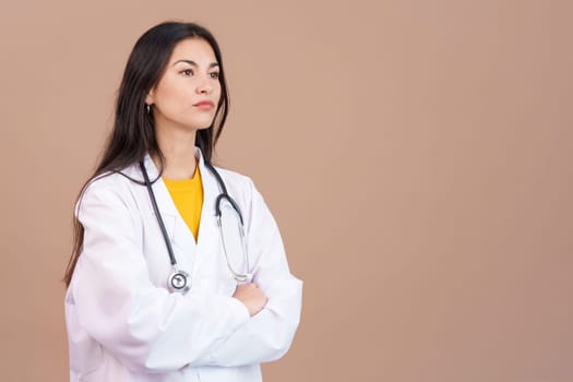 Serious hispanic female doctor with arms crossed looking away in studio with brown background