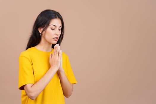 Caucasian woman praying with folded hands looking down in studio with brown background